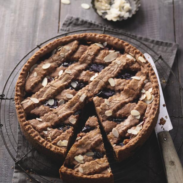 Eine Linzertorte mit Mandeln und einem herausgeschnittenen Stück auf einem grauen Tuch.
