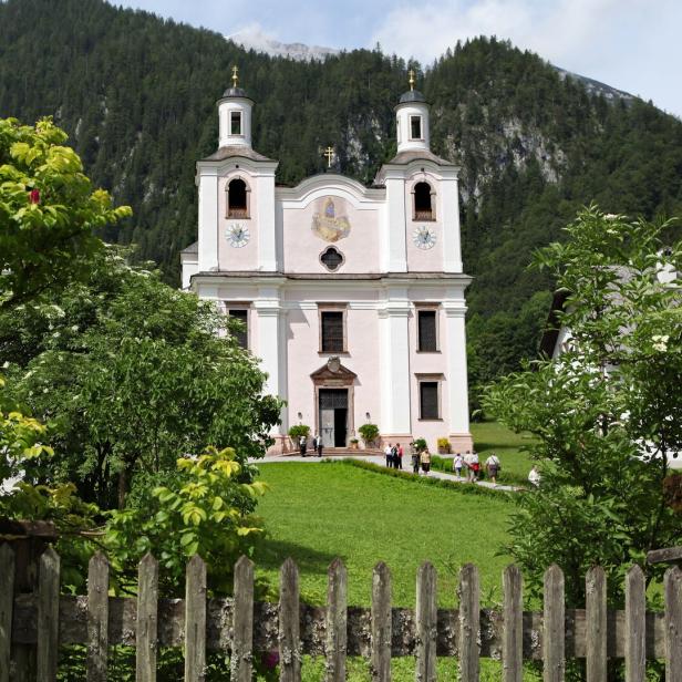Die Pfarrkirche St. Michael in Oberau vor einer bewaldeten Bergkulisse.