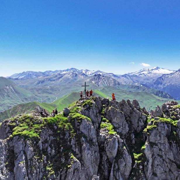 Bergsteiger genießen die Aussicht von einem felsigen Gipfel mit Gipfelkreuz.
