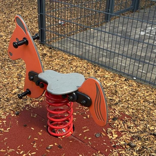 Ein orangefarbenes Schaukeltier in Pferdeform auf einem Spielplatz.