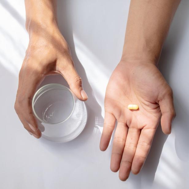Eine Hand mit einer Pille und einem Wasserglas.