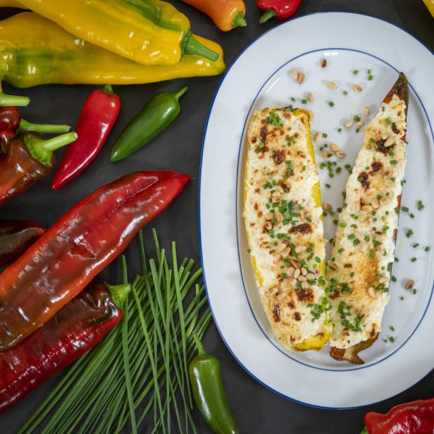 Gefüllte Paprika auf weißem Teller mit roten und gelben Paprikas und Schnittlauch rundherum