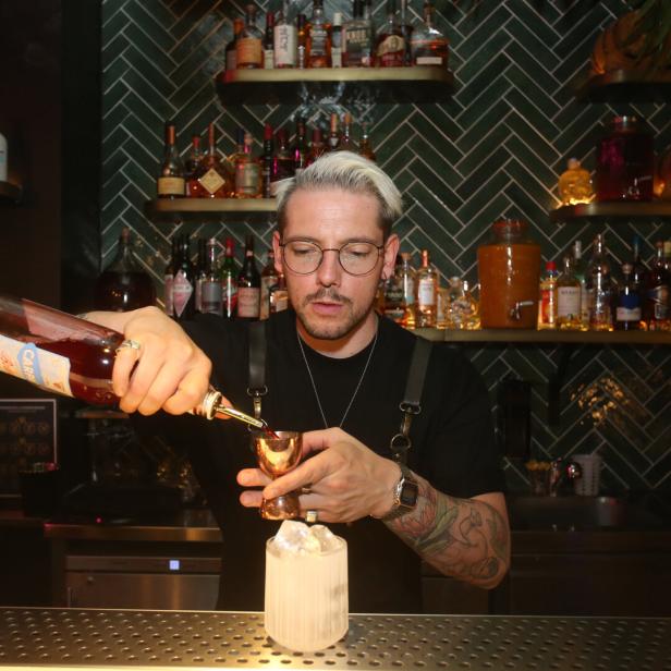 Ein Barkeeper mit Tätowierungen mixt einen Cocktail in einer Bar.