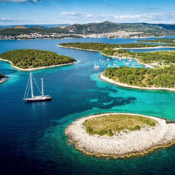 Eine Segelyacht ankert in einer Bucht mit türkisfarbenem Wasser und kleinen Inseln.