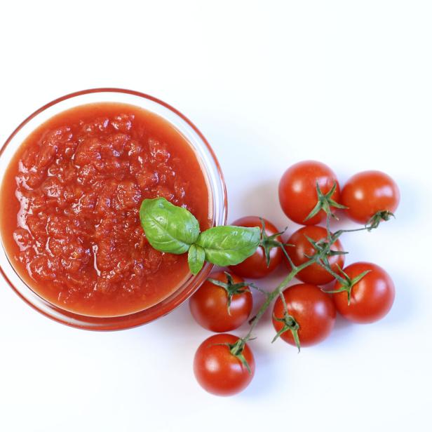 Eine Schüssel mit Tomatensauce, garniert mit Basilikum, neben einem Zweig Kirschtomaten.