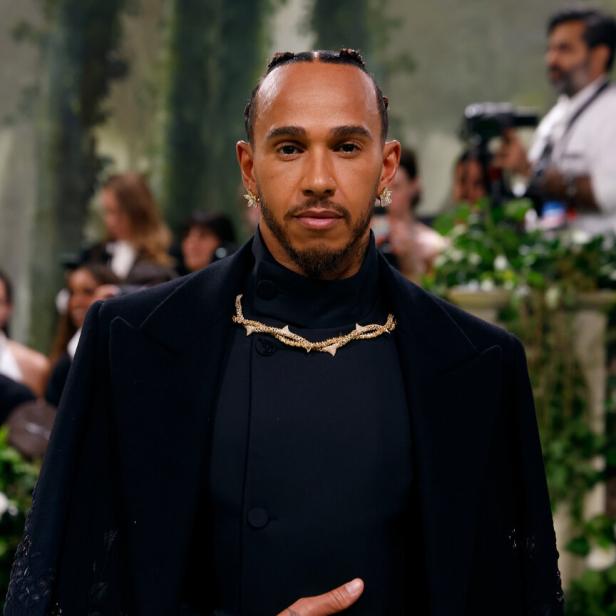 Lewis Hamilton trägt ein schwarzes Outfit mit goldenen Schmuckdetails.
