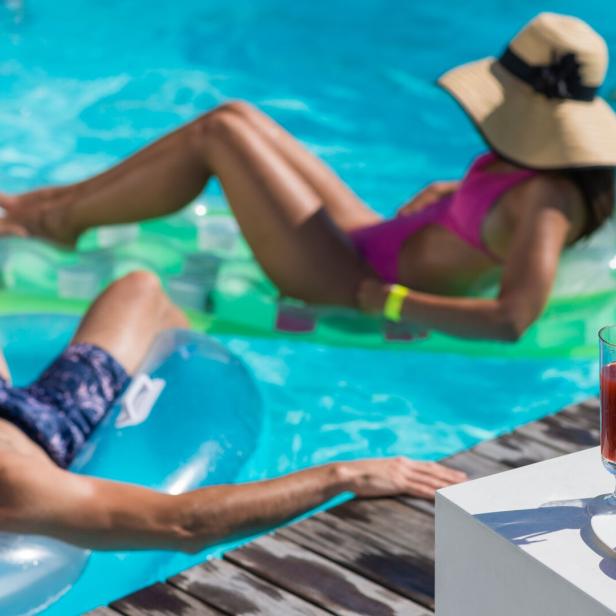 Menschen entspannen sich mit Getränken auf Schwimmreifen in einem Pool.