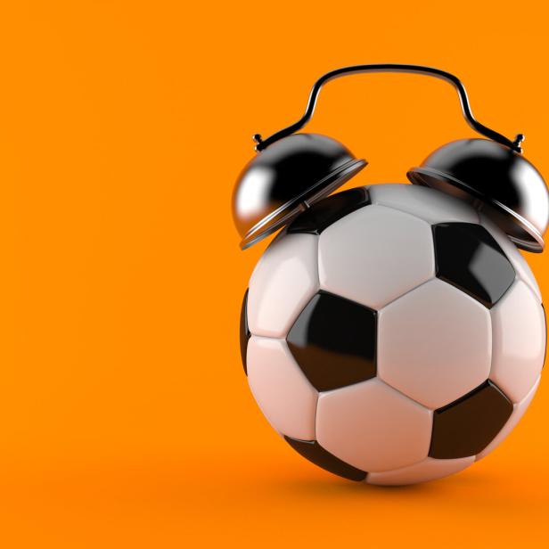 Ein Wecker mit einem Fußball als Zifferblatt vor orangefarbenem Hintergrund.