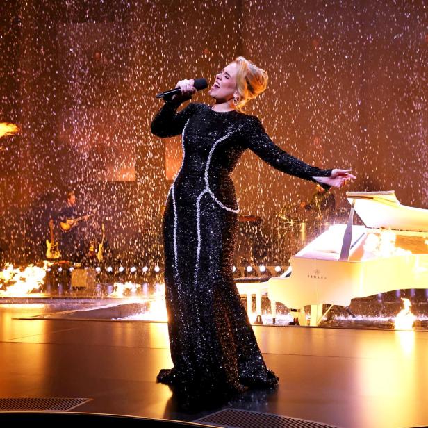 Adele singt auf einer Bühne mit einem weißen Klavier und Feuereffekten.