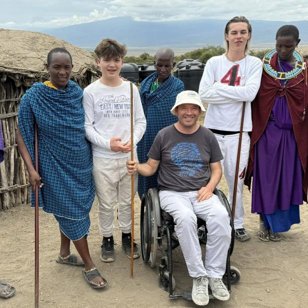 Ein Mann im Rollstuhl posiert mit einer Gruppe von Massai in traditioneller Kleidung.
