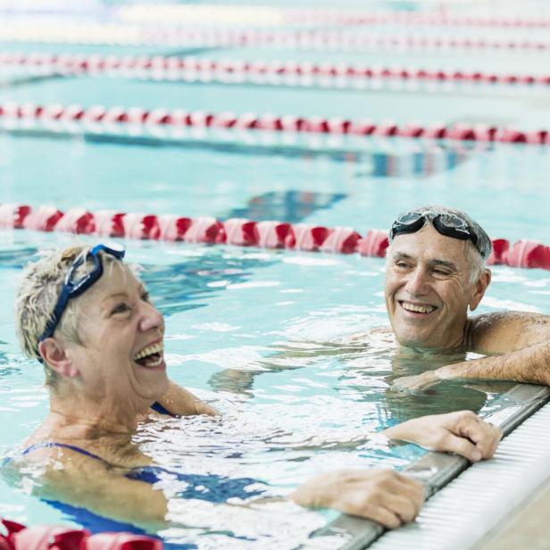 Ein älterer Mann und eine ältere Frau lehnen im Schwimmbecken am Rand.