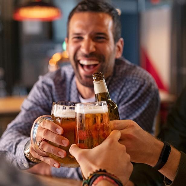 Drei Männer stoßen in einer Bar mit Bierkrügen an.