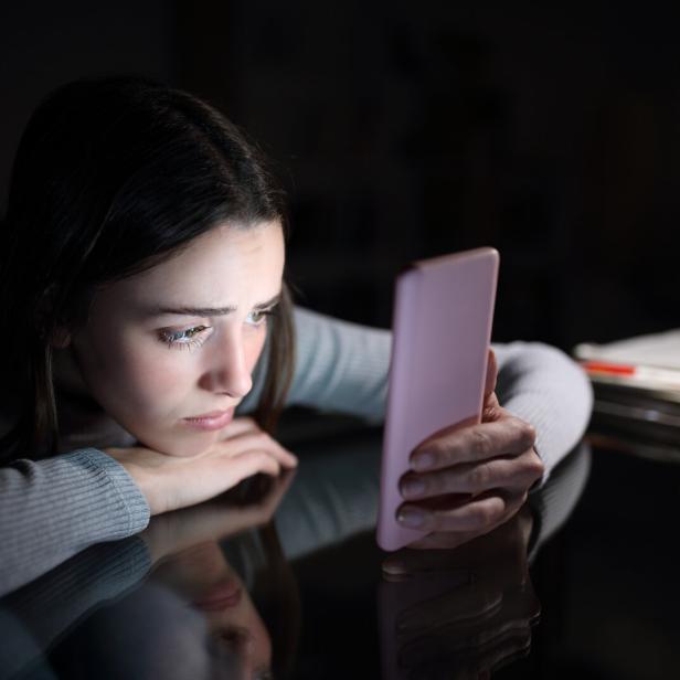Frau schaut traurig auf ihr Smartphone.