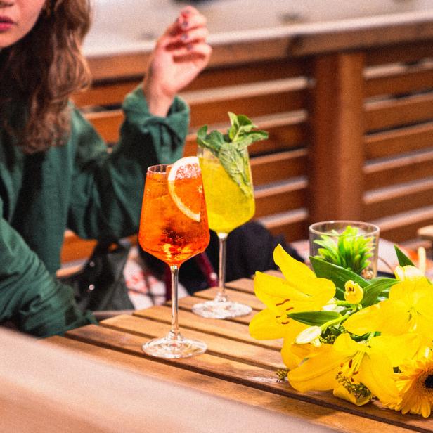 Zwei Frauen sitzen an einem Tisch mit Getränken und gelben Blumen.