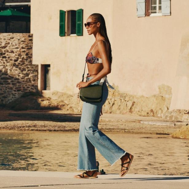 Eine Frau mit Sonnenbrille und Handtasche geht am Strand entlang.