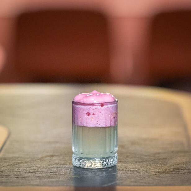 Ein Glas mit einem rosa Getränk steht auf einem Tisch.
