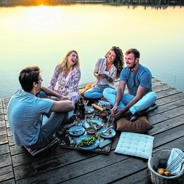 Eine Gruppe Freunde genießt ein Picknick auf einem Holzsteg am See.
