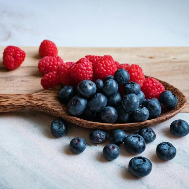 Himbeeren und Blaubeeren liegen auf einem Holzlöffel.