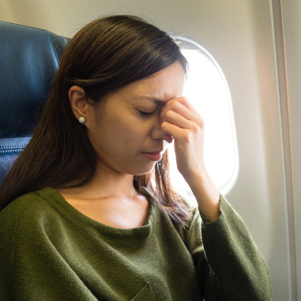 Eine Frau sitzt ängstlich im Flugzeug und hält sich die Stirn.