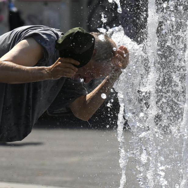 Ein Mann erfrischt sich an einem heißen Tag an einem Springbrunnen.