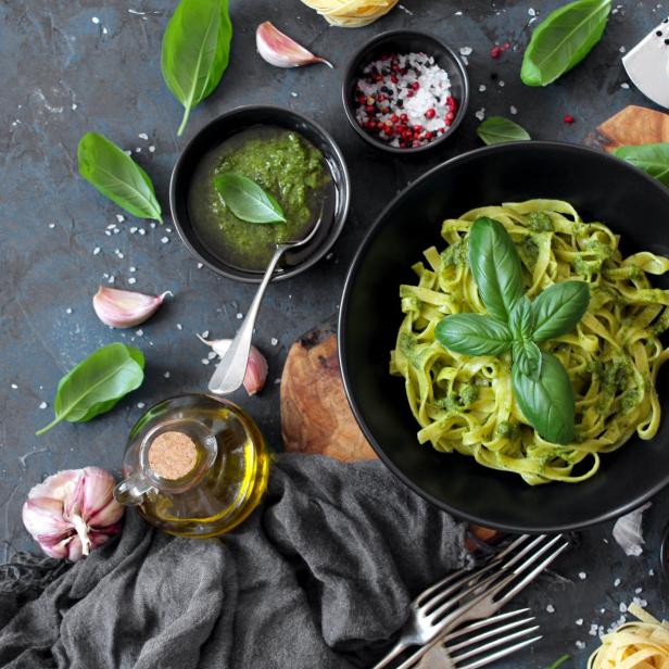 Pasta-Tagliatelle mit Pesto und frischen Basilikumblättern in einer schwarzen Schüssel.