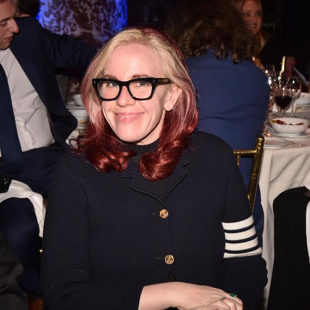Eine Frau mit blond-roten Haaren und Brille sitzt an einem Tisch.