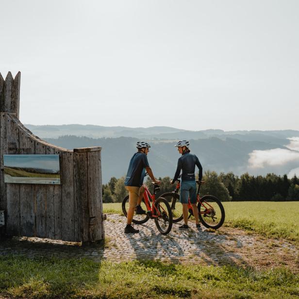 Zwei Radfahrer machen eine Pause an einem Aussichtspunkt mit Blick auf die Landschaft.
