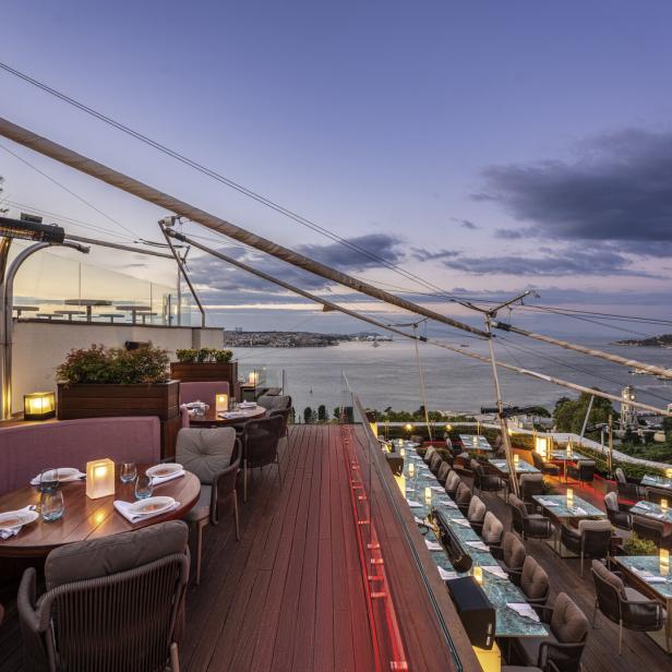 Ein Restaurant mit Tischen und Stühlen bietet einen Panoramablick auf das Meer bei Sonnenuntergang.