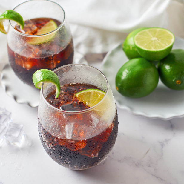 Zwei Gläser Cuba Libre mit Limetten und Eiswürfeln auf einem Tisch.