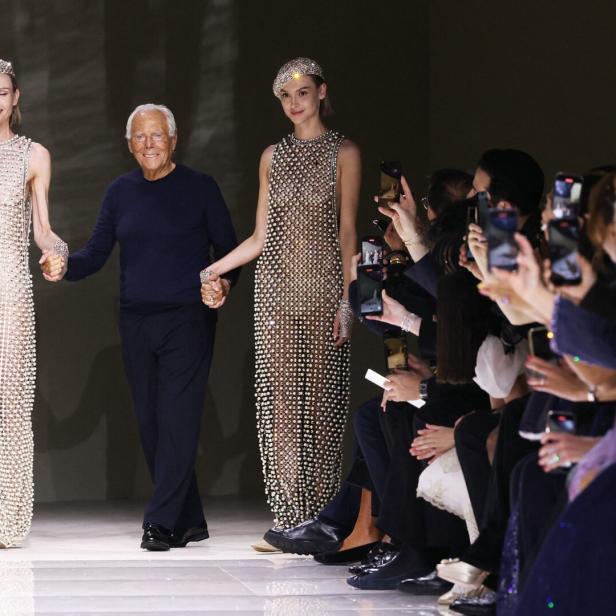 Giorgio Armani führt zwei Models in perlenbesetzten Kleidern über den Laufsteg.