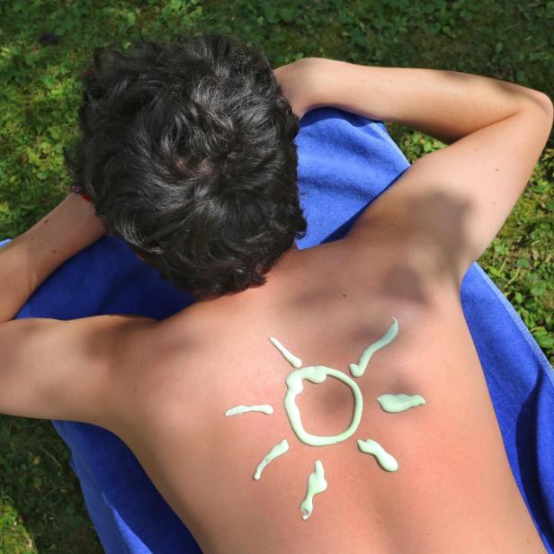 Ein Mann liegt mit Sonnencreme-Sonne auf dem Rücken auf einem Handtuch im Gras.