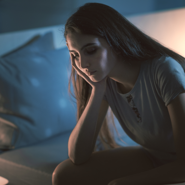 Frau sitzt nachdenklich im Bett und kann nicht schlafen.
