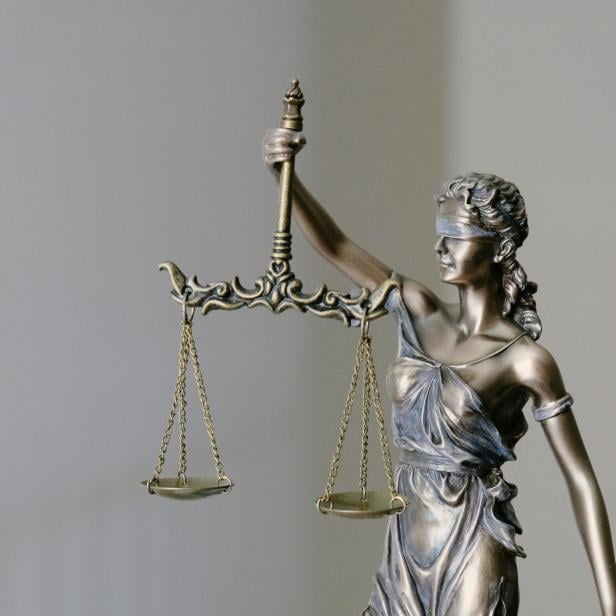 Eine bronzene Justitia-Figur mit Augenbinde hält eine Waage in der erhobenen rechten Hand.