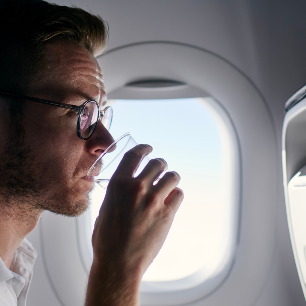 Mann sitzt im Flugzeug und trinkt Wasser.