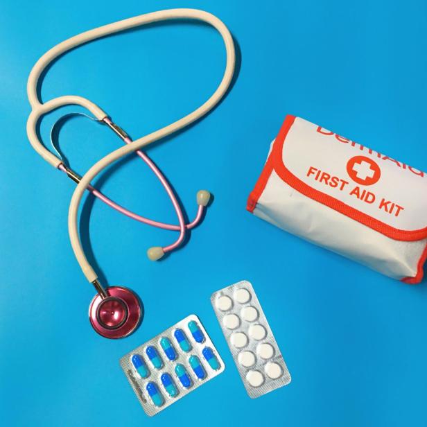 Ein Erste-Hilfe-Kasten, ein Stethoskop und Tabletten auf blauem Hintergrund.