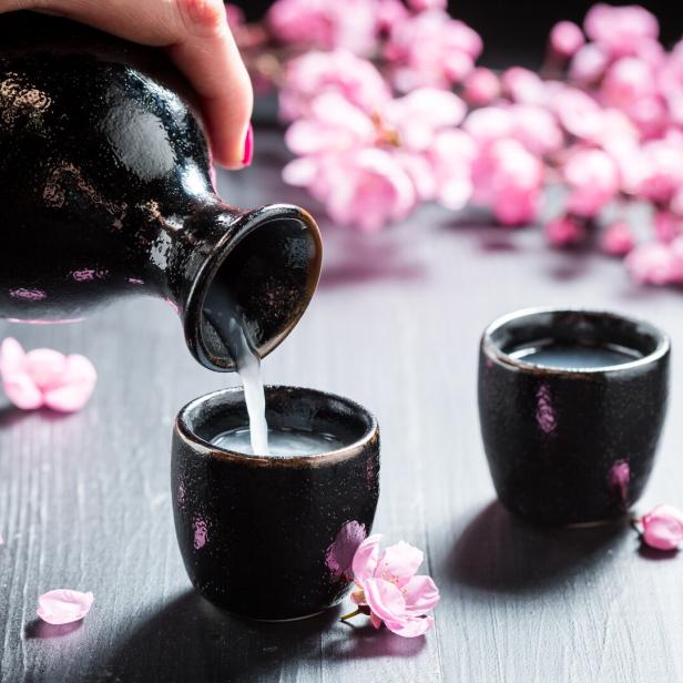 Sake wird in ein kleines Gefäß gegossen, im Hintergrund rosa Blüten.