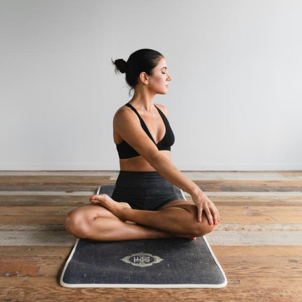 Eine Frau sitzt in Lotusposition auf einer Yogamatte und meditiert.