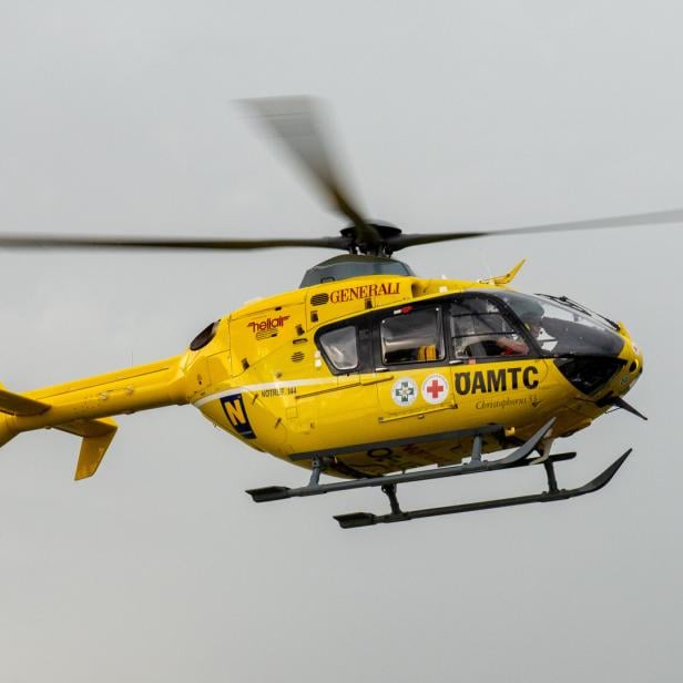 Ein gelber ÖAMTC Hubschrauber fliegt vor einem grauen Himmel.