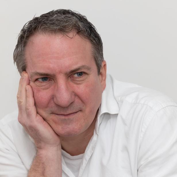 Ein Mann in einem weißen Hemd stützt sein Gesicht mit der Hand ab.