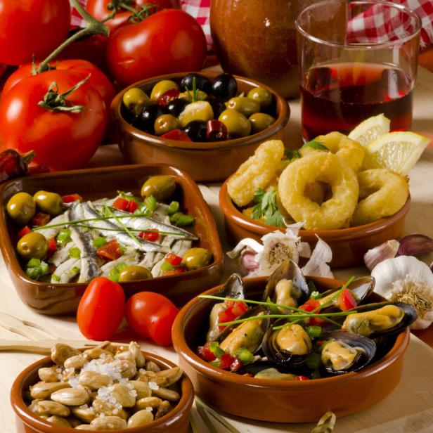 Verschiedene Tapas, darunter Oliven, Sardellen, Calamari und Muscheln, werden auf einem Tisch präsentiert.