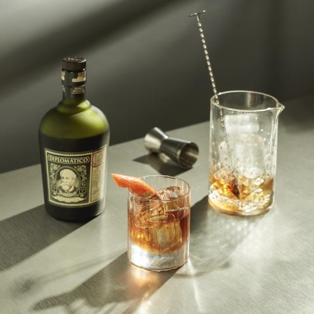 Ein Cocktail mit Eis und Orangenzeste neben einer Flasche Diplomático Rum.