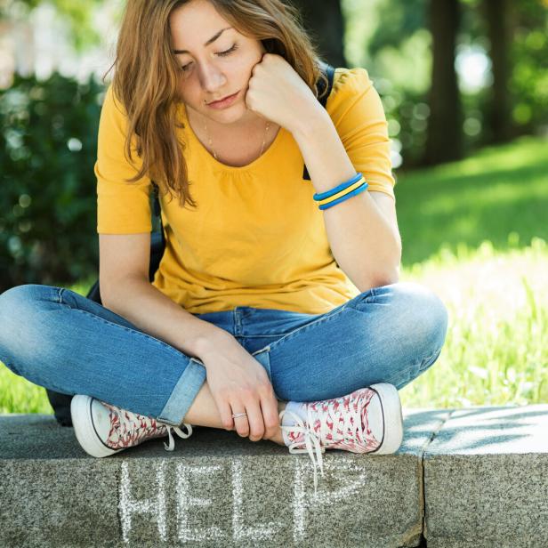 Ein trauriges Mädchen sitzt auf einer Mauer.