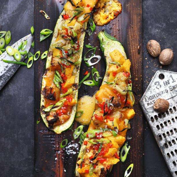 Gefüllte Zucchini mit Käse und Gemüse auf einem Holzbrett.