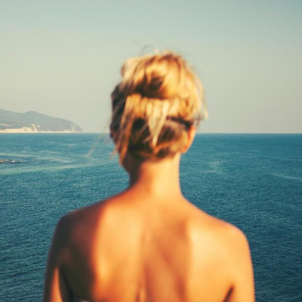 Eine Frau blickt auf das Meer und die Küste.