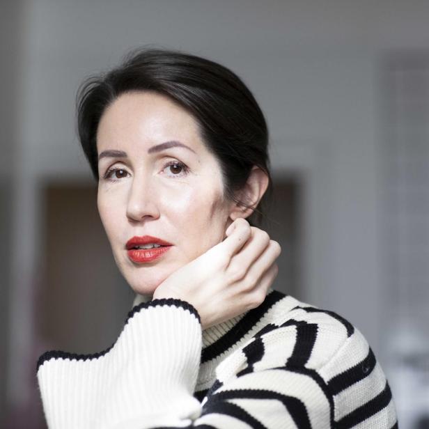 Eine Frau mit dunklen Haaren und rotem Lippenstift trägt einen schwarz-weiß gestreiften Pullover.