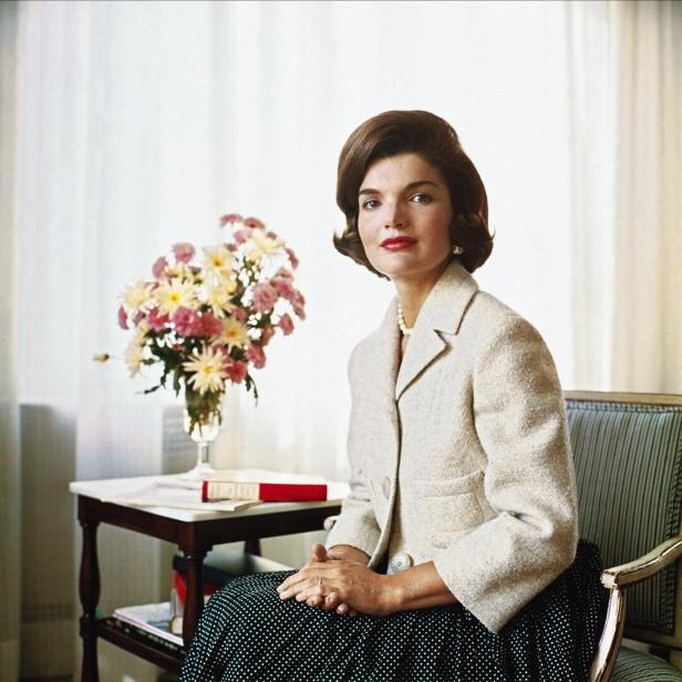 Ein Porträt von Jackie Kennedy in einem Tweed-Kostüm neben einem Blumenarrangement.
