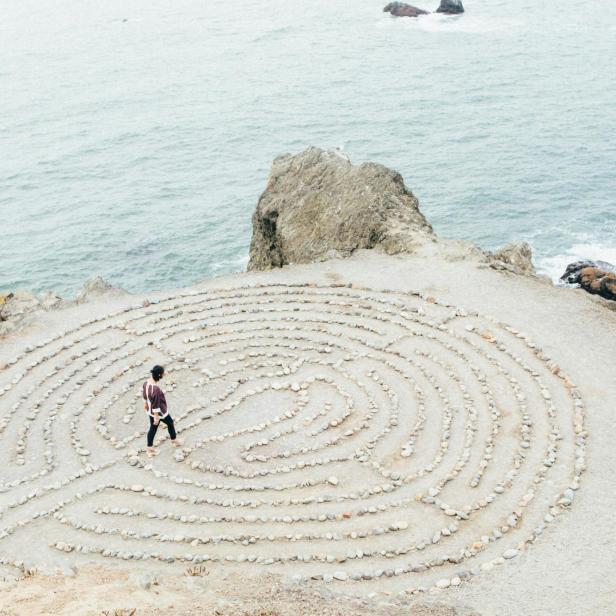 Eine Person geht durch ein Steinlabyrinth auf einer Klippe am Meer.