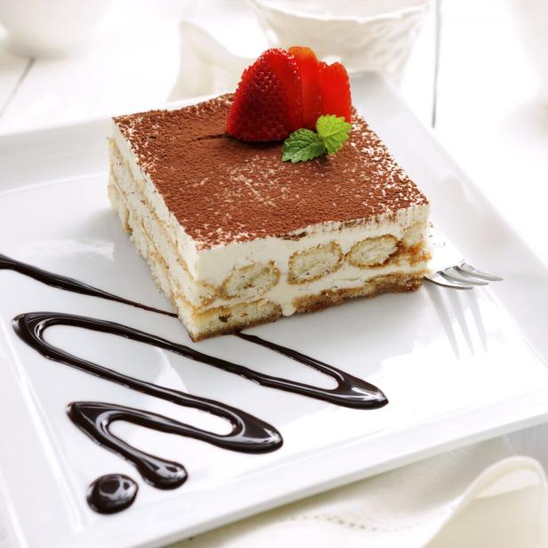 Ein Stück Tiramisu ist mit Erdbeeren und Schokoladensoße verziert.