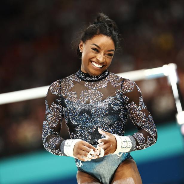 Simone Biles lächelt bei einem Gymnastikwettkampf.