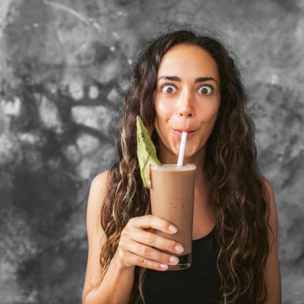 Eine Frau trinkt einen Smoothie mit einem Strohhalm und macht ein lustiges Gesicht.